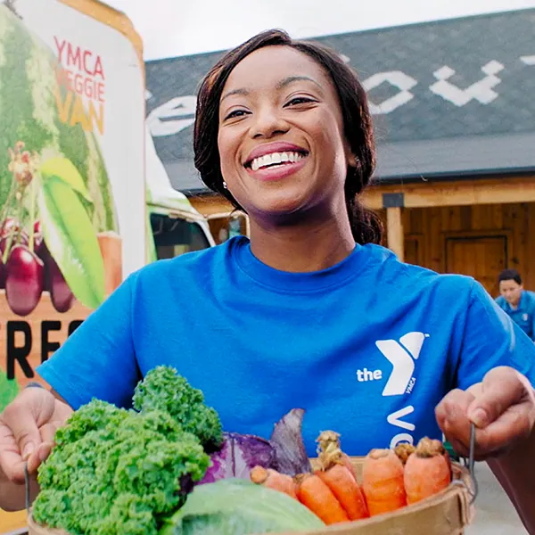 Smiling YMCA staff member holding a basket of fresh vegetables